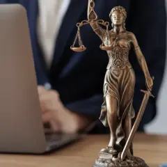 Justitia-Statue neben Laptop und Büchern. Ein Anwalt prüft Unterlagen, vielleicht wegen eines Widerspruchs Pflegegrad.