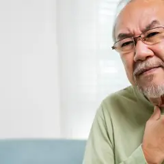Älterer Mann mit Brille fasst sich an den Hals, deutet auf Probleme beim **Verschlucken im Alter**.