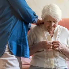 Eine Person hilft einer älteren Dame beim Anziehen, was die Prinzipien des Bobath-Konzepts widerspiegelt, um Selbstständigkeit zu fördern.