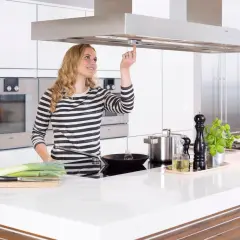 Junge Frau bedient Dunstabzugshaube mit Herd-Abschaltautomatik. Sicheres Kochen für Senioren.